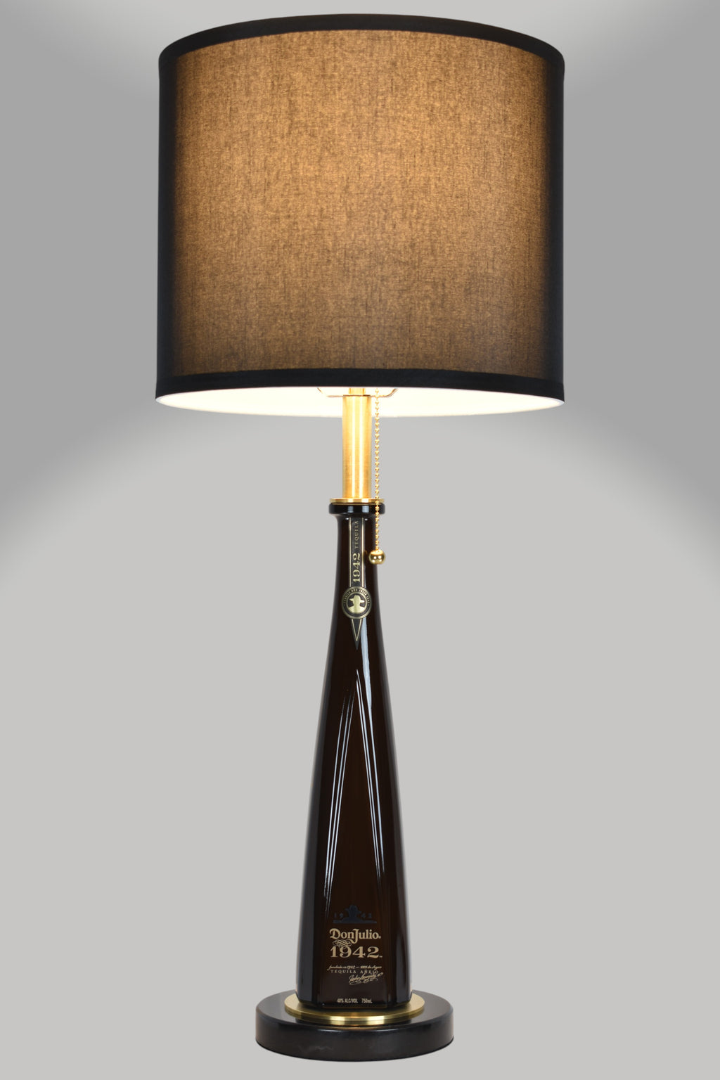 Liquor bottle lamp made from a reclaimed Don Julio 1942 Tequila bottle, full view, light on, on a gray background