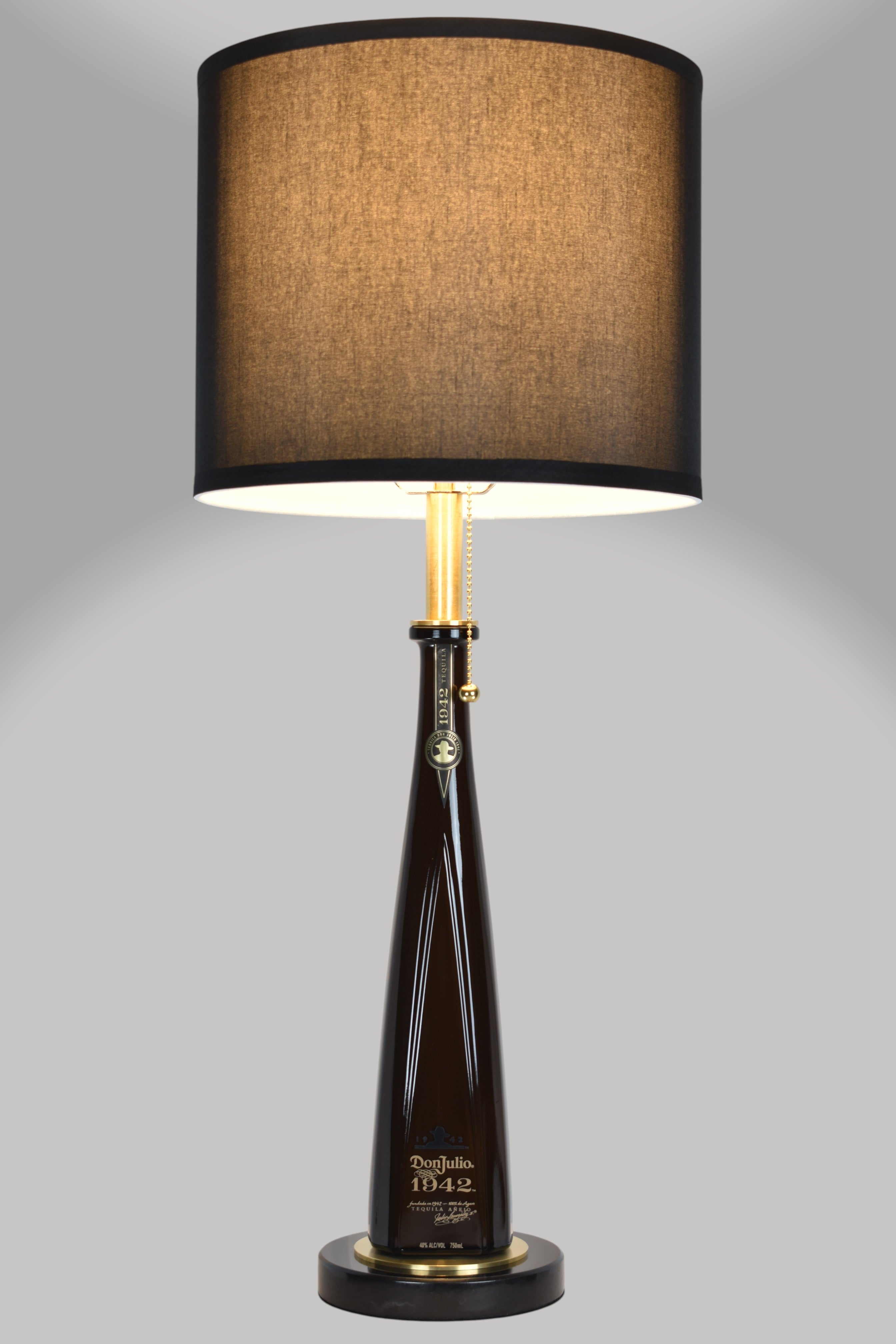Liquor bottle lamp made from a reclaimed Don Julio 1942 Tequila bottle, full view, light on, on a gray background