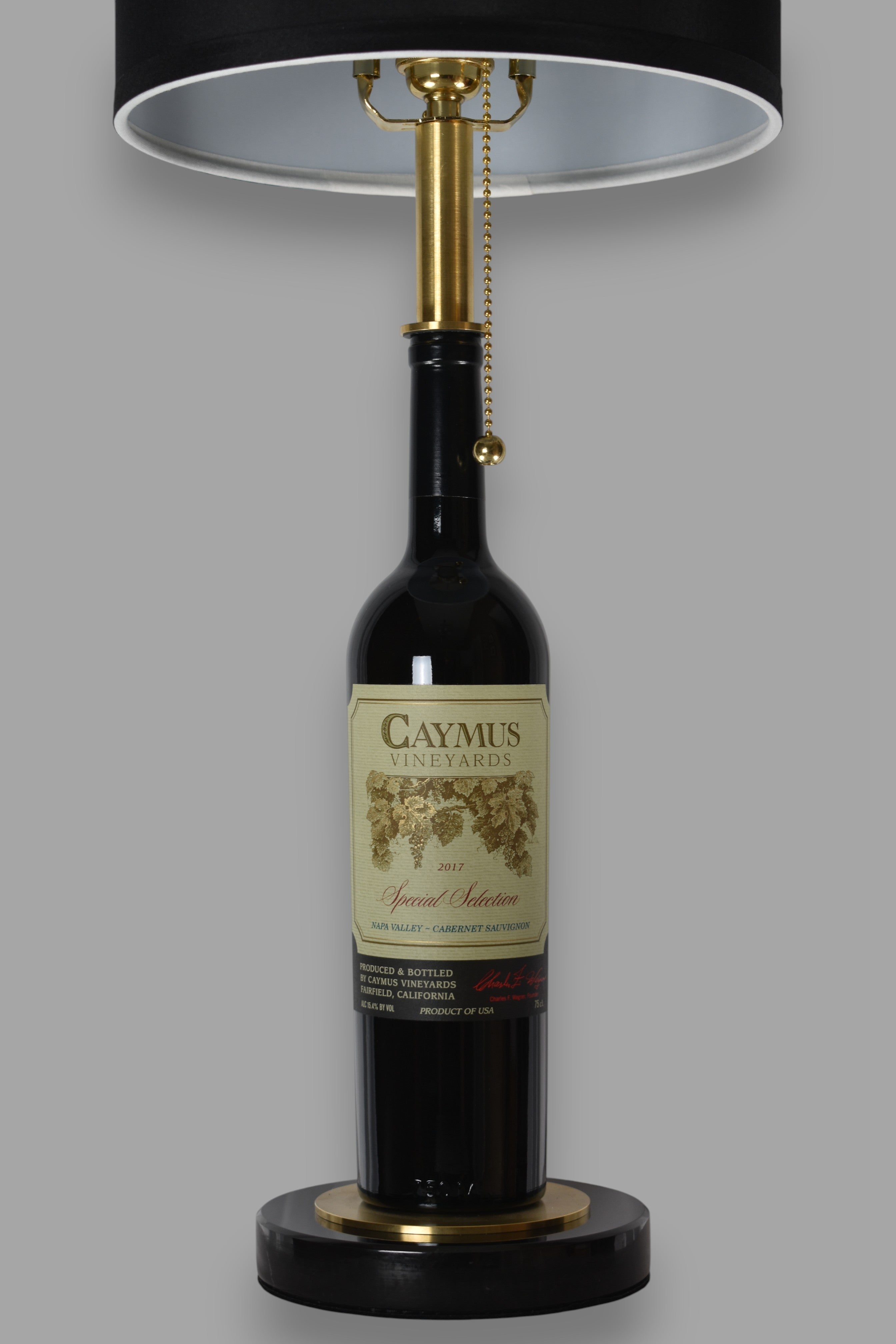 Wine bottle lamp made from a reclaimed 2017 Caymus Cabernet Sauvignon bottle, front view, on a gray background