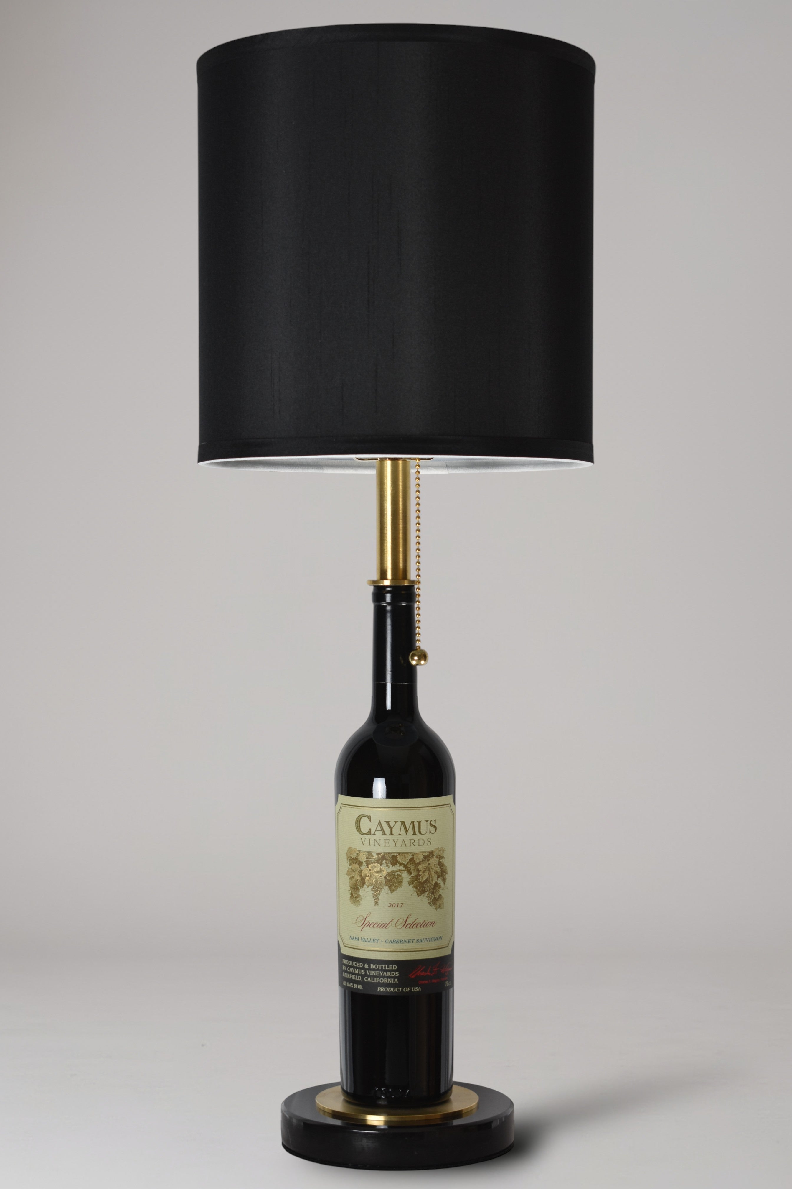 Wine bottle lamp made from a reclaimed 2017 Caymus Cabernet Sauvignon bottle, full view, light off, on a gray background