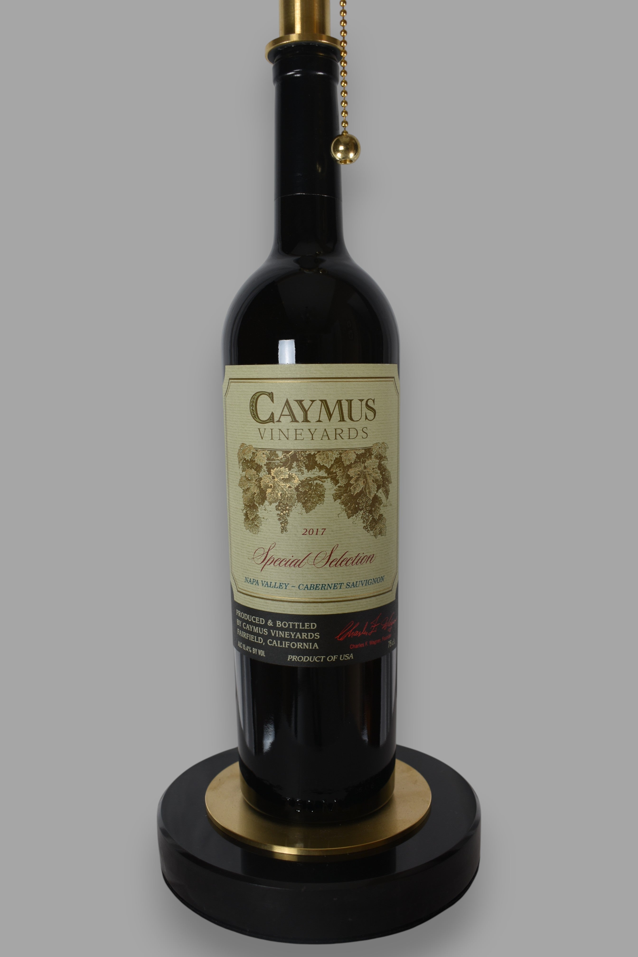 Wine bottle lamp made from a reclaimed 2017 Caymus Cabernet Sauvignon bottle, close-up view, on a gray background