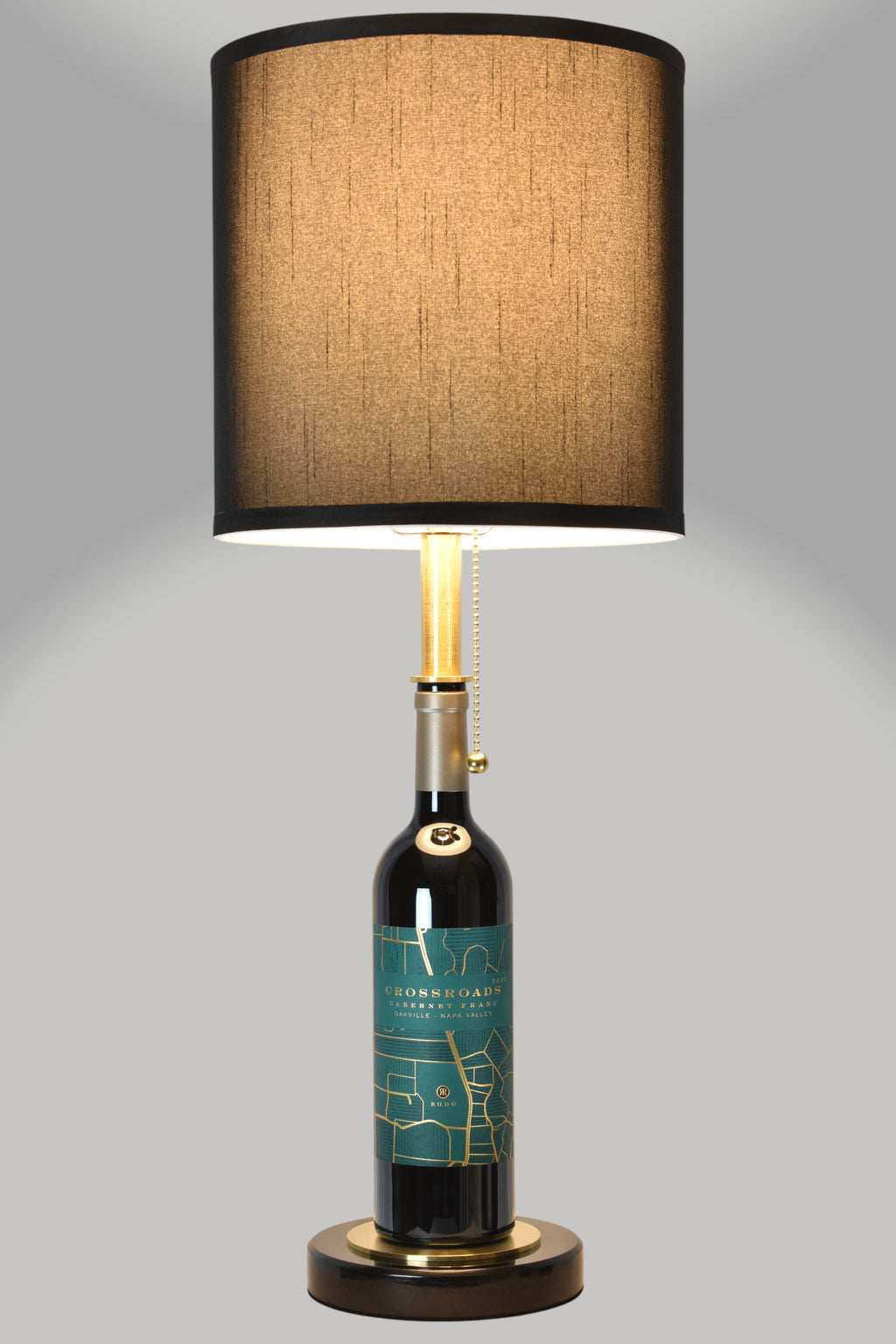 Wine bottle lamp made from a reclaimed 2022 Crossroads Cabernet Franc bottle, full view, light on, on a gray background