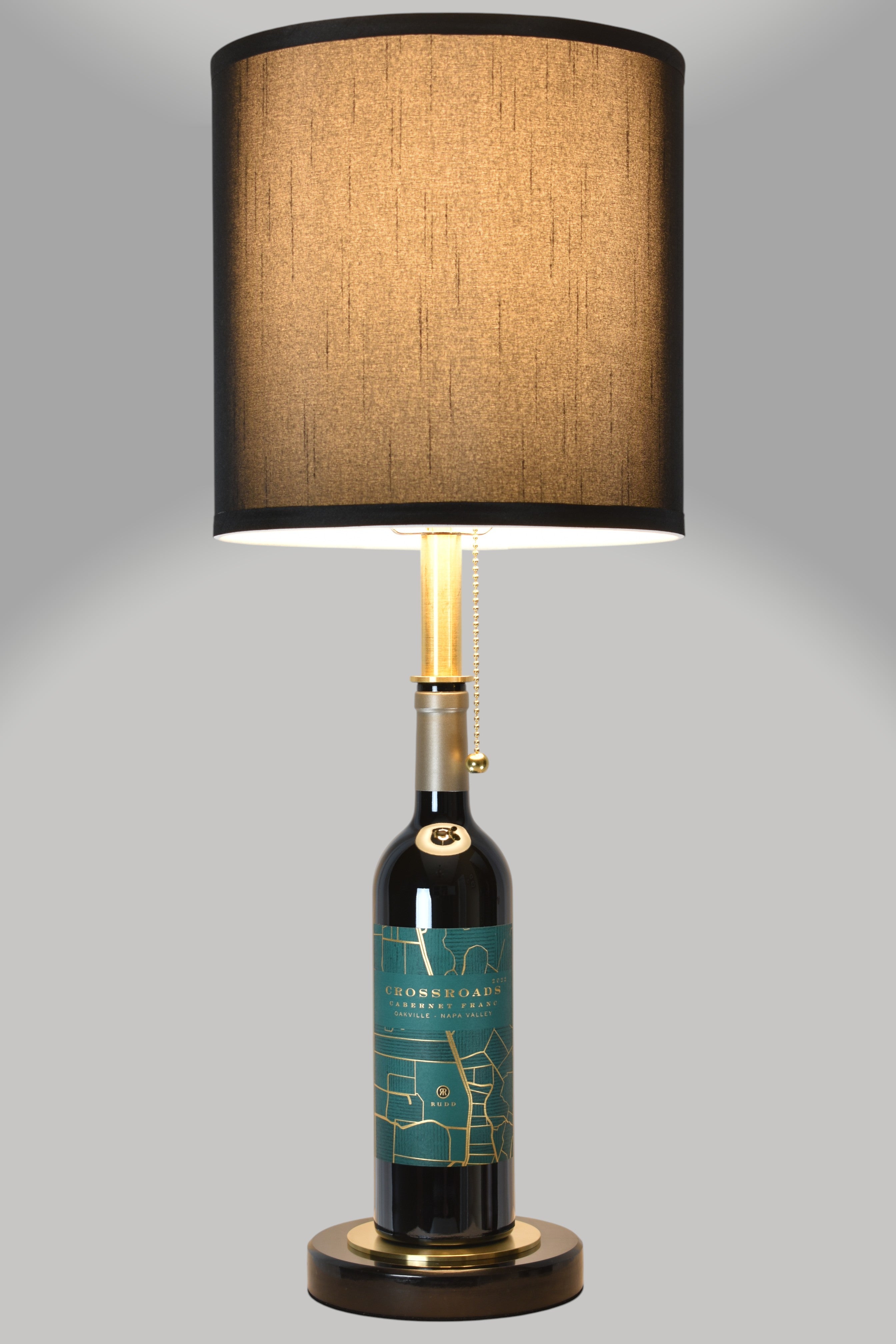 Wine bottle lamp made from a reclaimed 2022 Crossroads Cabernet Franc bottle, full view, light on, on a gray background