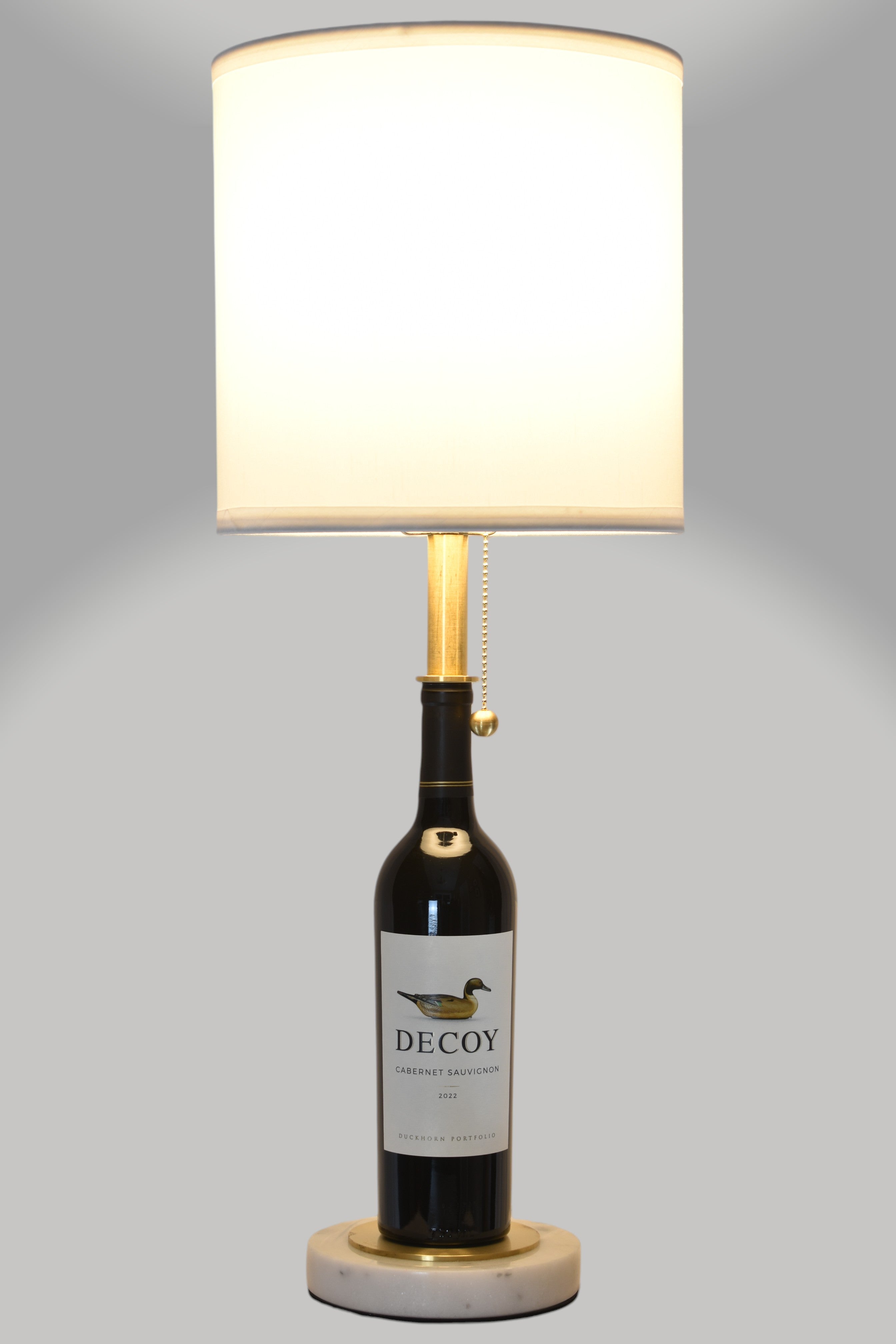 Wine bottle lamp made from a reclaimed 2022 Decoy Cabernet Sauvignon bottle, full view, light on, on a gray background