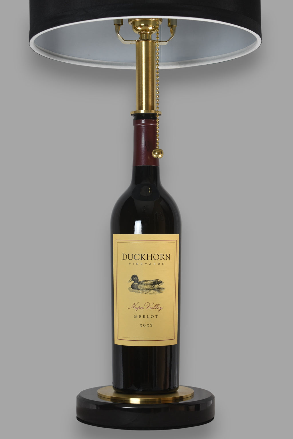 Wine bottle lamp made from a reclaimed 2022 Duckhorn Merlot bottle, front view, on a gray background