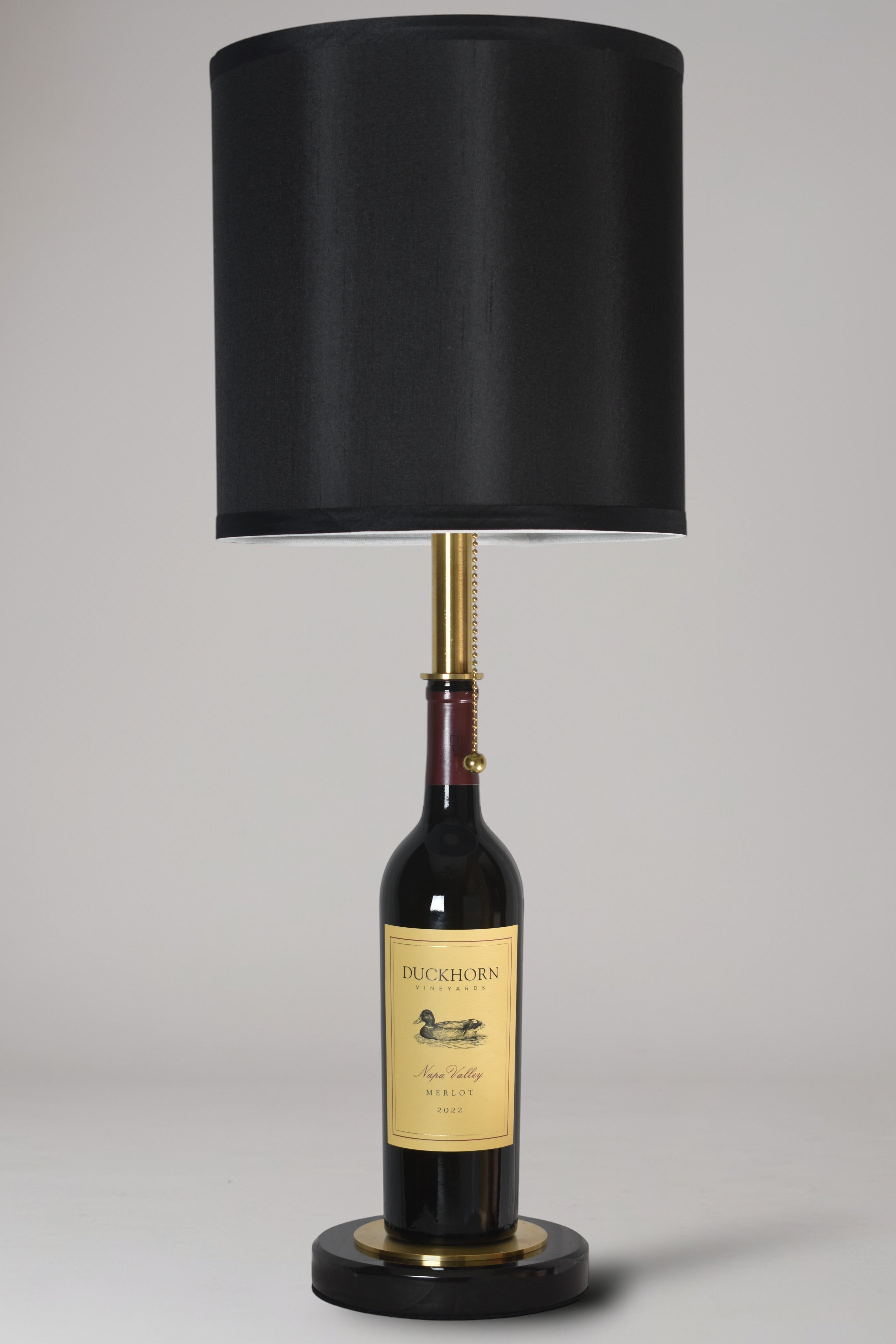 Wine bottle lamp made from a reclaimed 2022 Duckhorn Merlot bottle, full view, light off, on a gray background