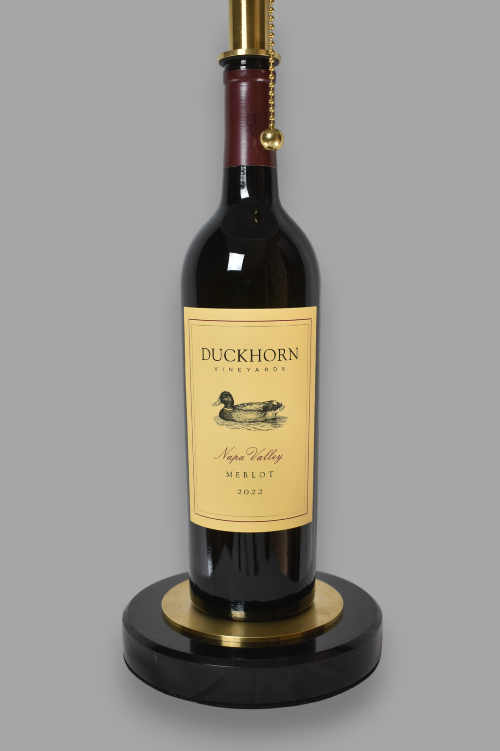 Wine bottle lamp made from a reclaimed 2022 Duckhorn Merlot bottle, close-up view, on a gray background