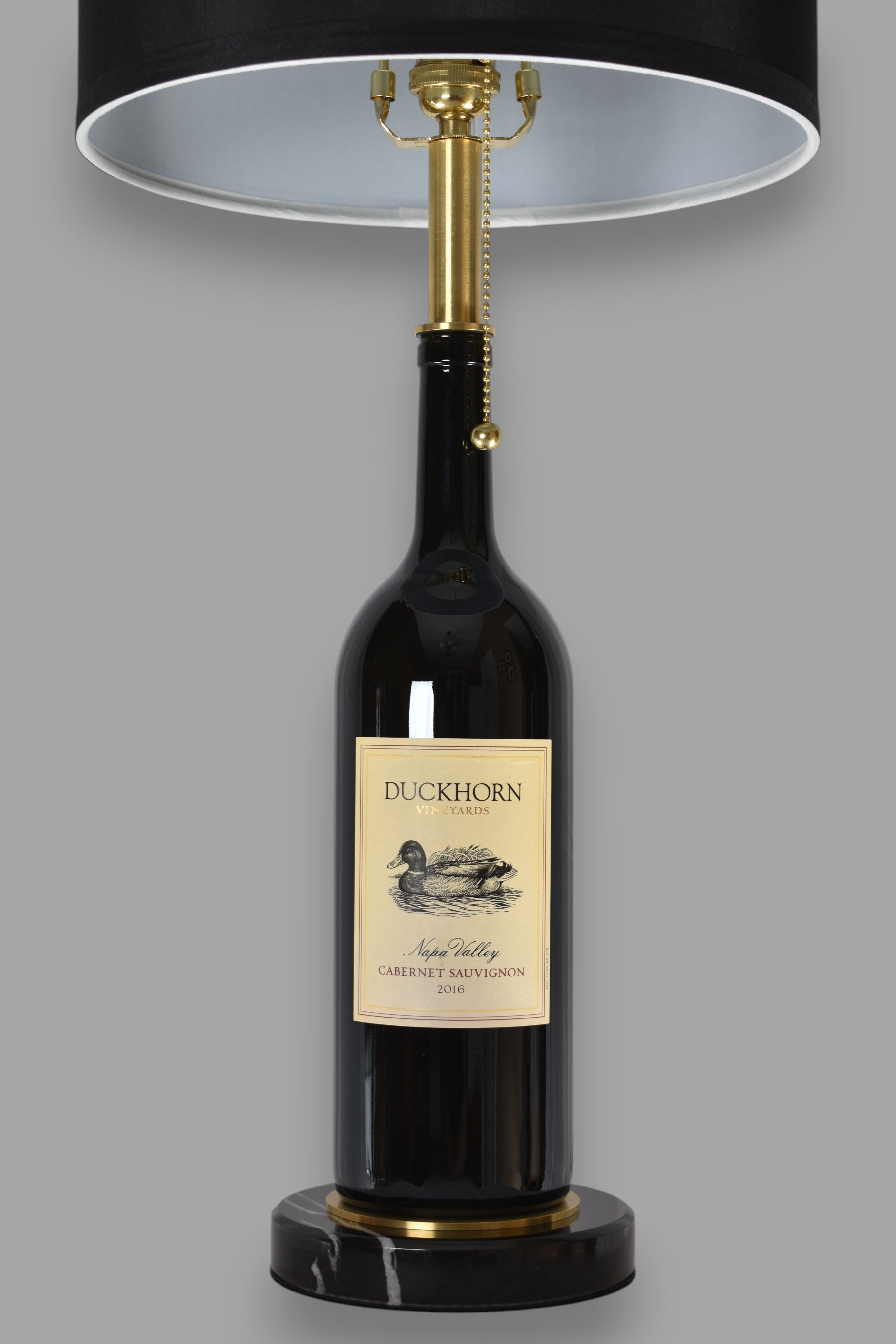 Wine bottle lamp made from a reclaimed 2016 Duckhorn Magnum Cabernet Sauvignon bottle, front view, on a gray background
