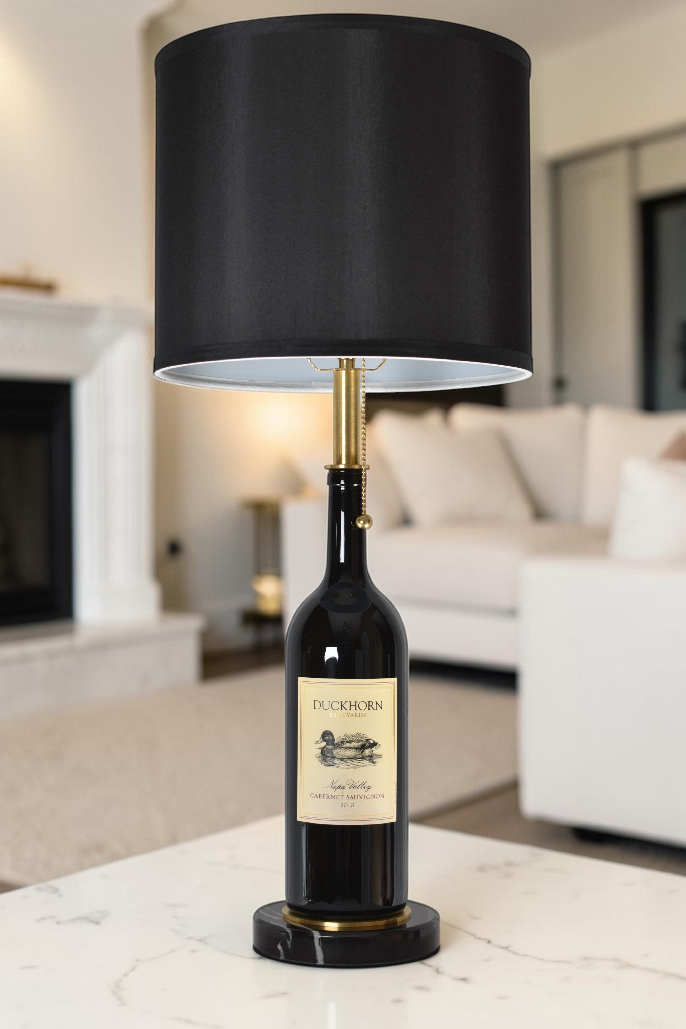 Wine bottle lamp made from a reclaimed 2016 Duckhorn Magnum Cabernet Sauvignon bottle, full view, light off, in a cozy living room