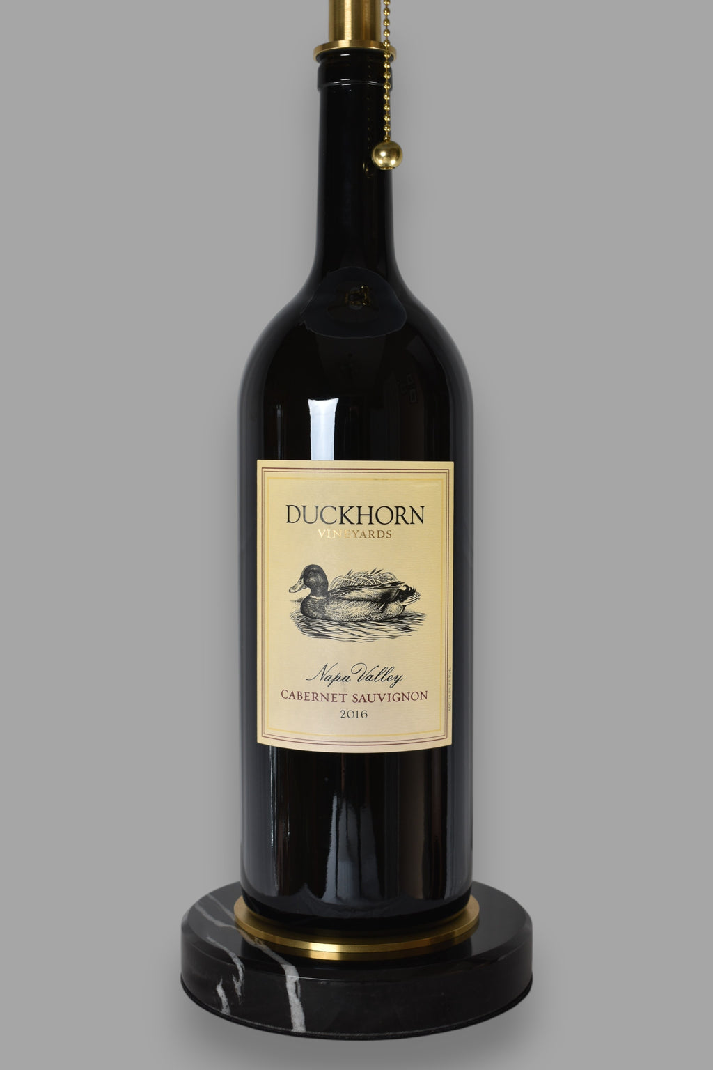 Wine bottle lamp made from a reclaimed 2016 Duckhorn Magnum Cabernet Sauvignon bottle, close-up view, on a gray background
