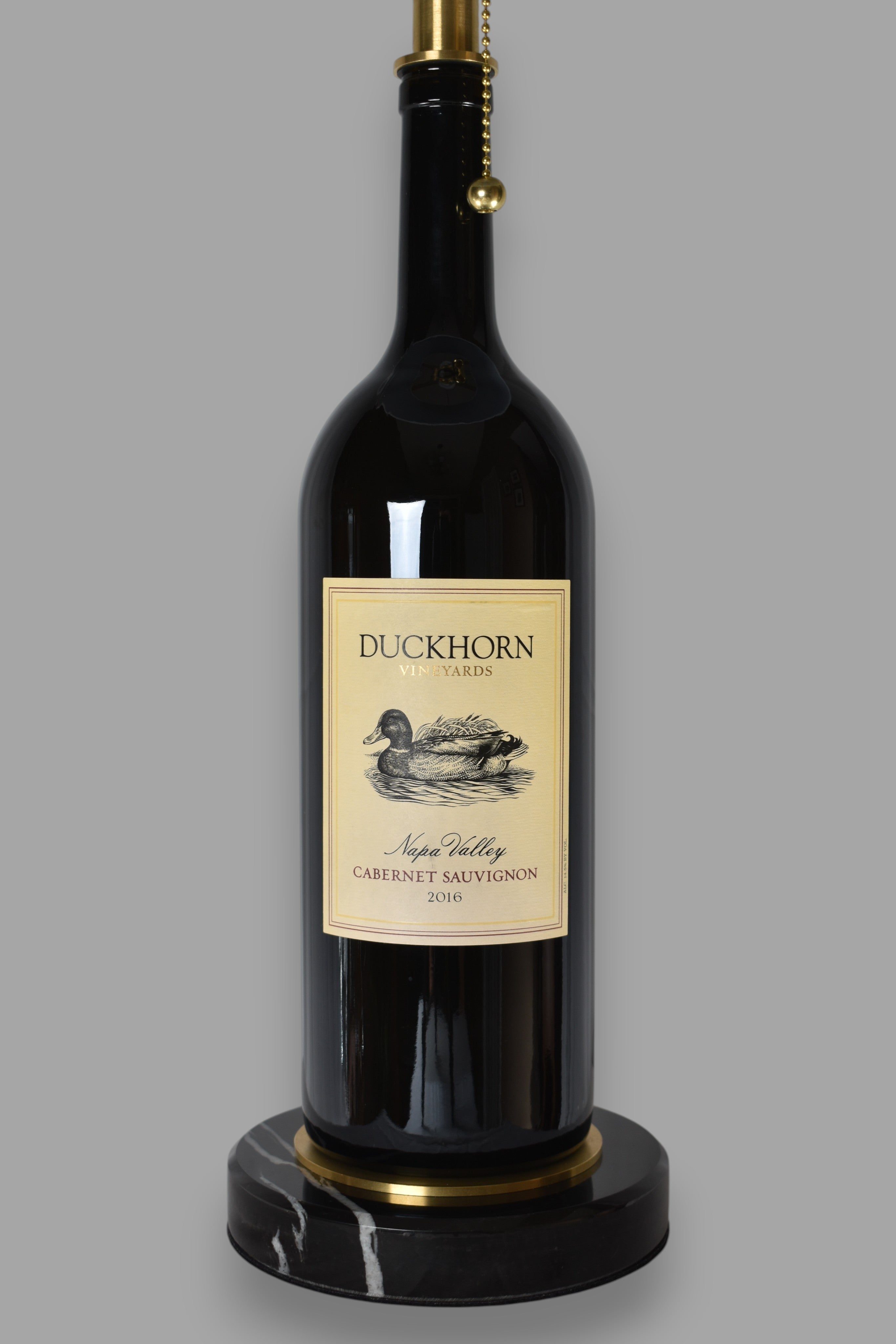 Wine bottle lamp made from a reclaimed 2016 Duckhorn Magnum Cabernet Sauvignon bottle, close-up view, on a gray background