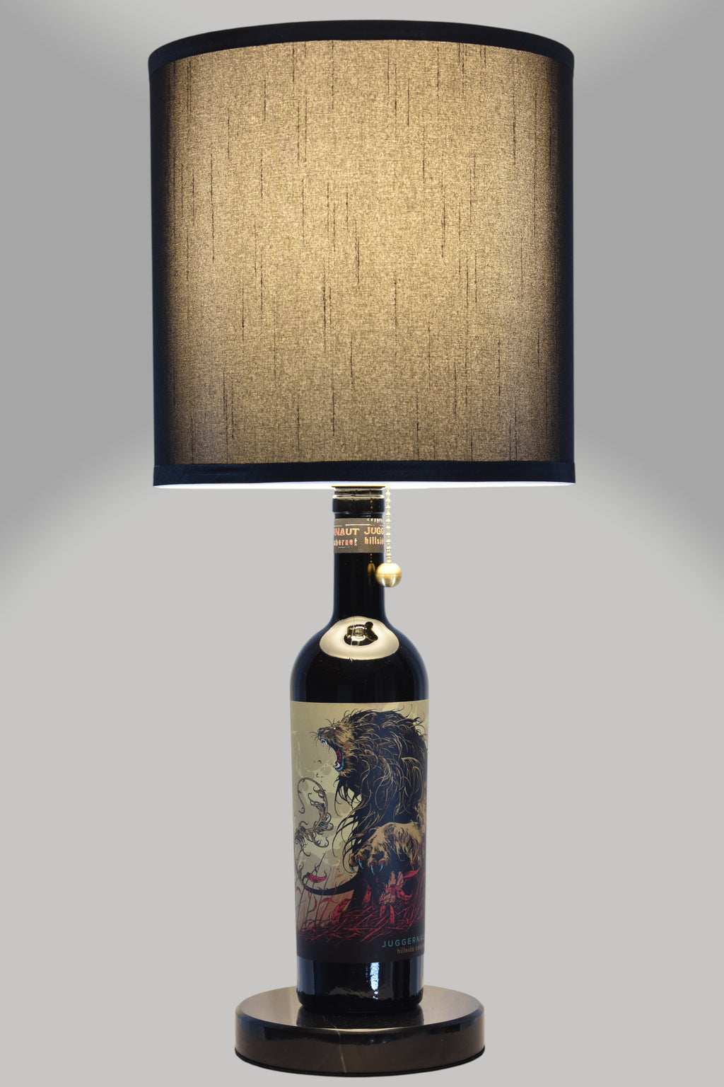 Wine bottle lamp made from a reclaimed Juggernaut Cabernet Sauvignon bottle, full view, light on, on a gray background