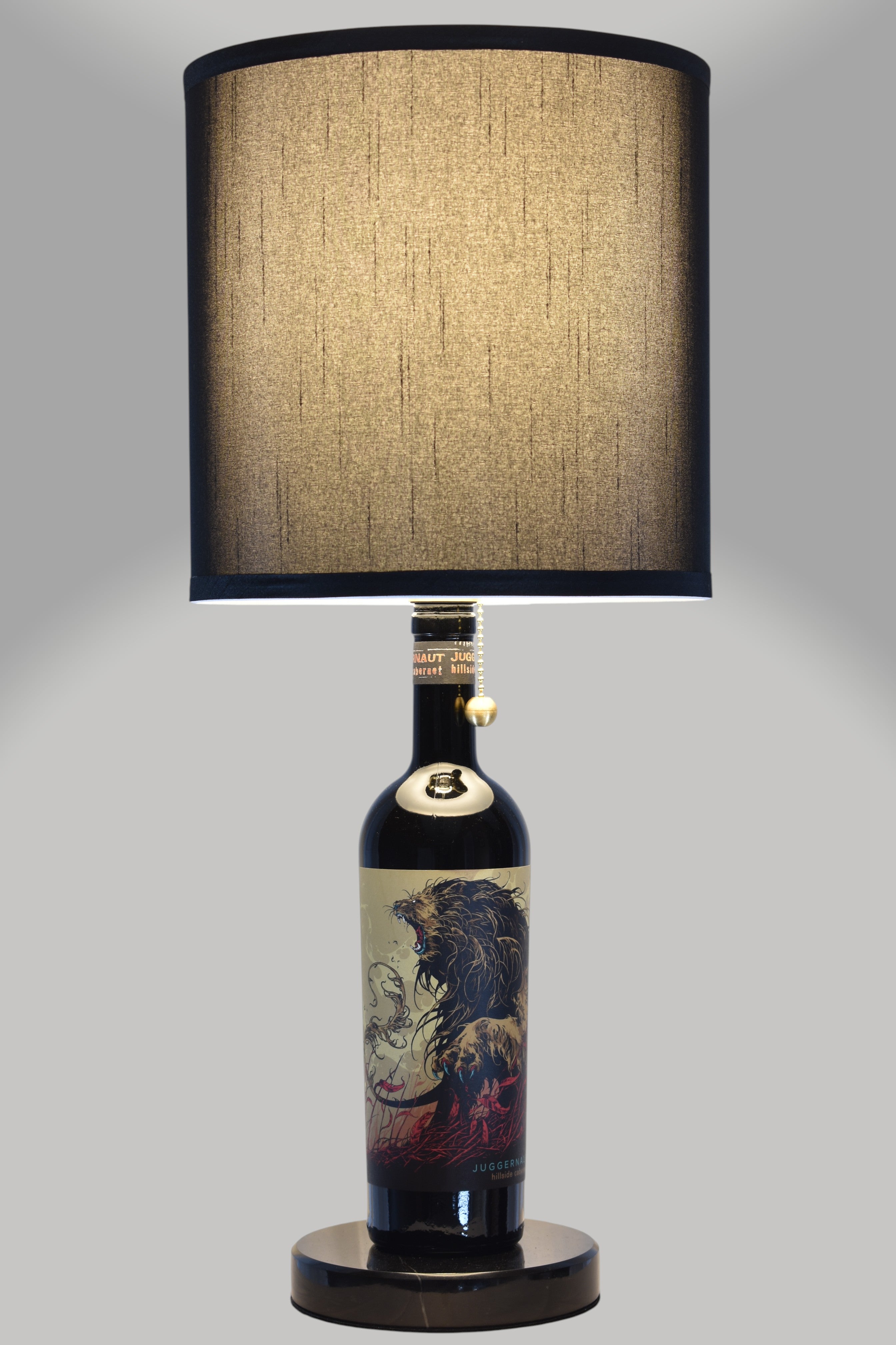 Wine bottle lamp made from a reclaimed Juggernaut Cabernet Sauvignon bottle, full view, light on, on a gray background