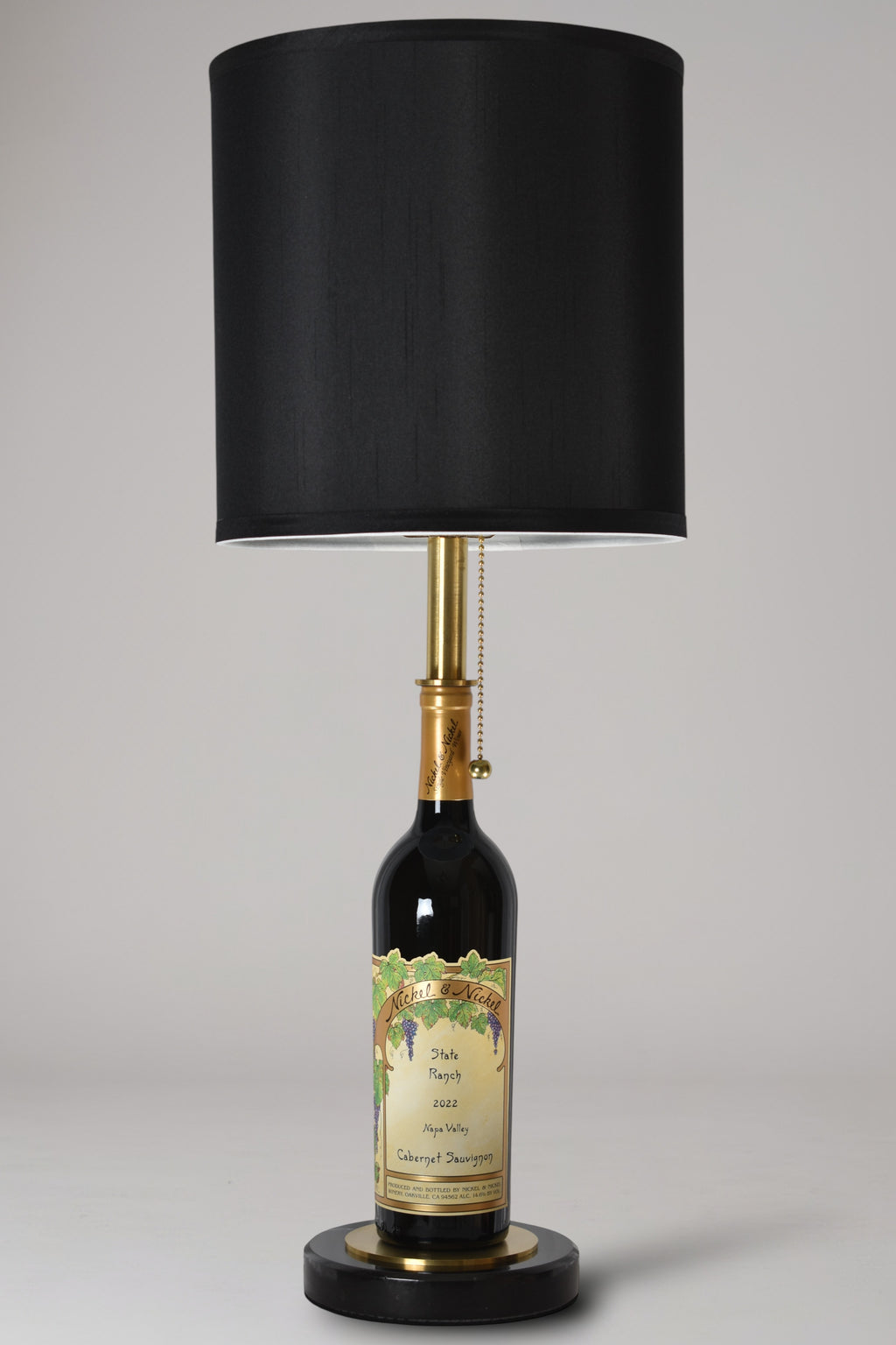 Wine bottle lamp made from a reclaimed 2022 Nickel & Nickel Cabernet Sauvignon bottle, full view, light off, on a gray background
