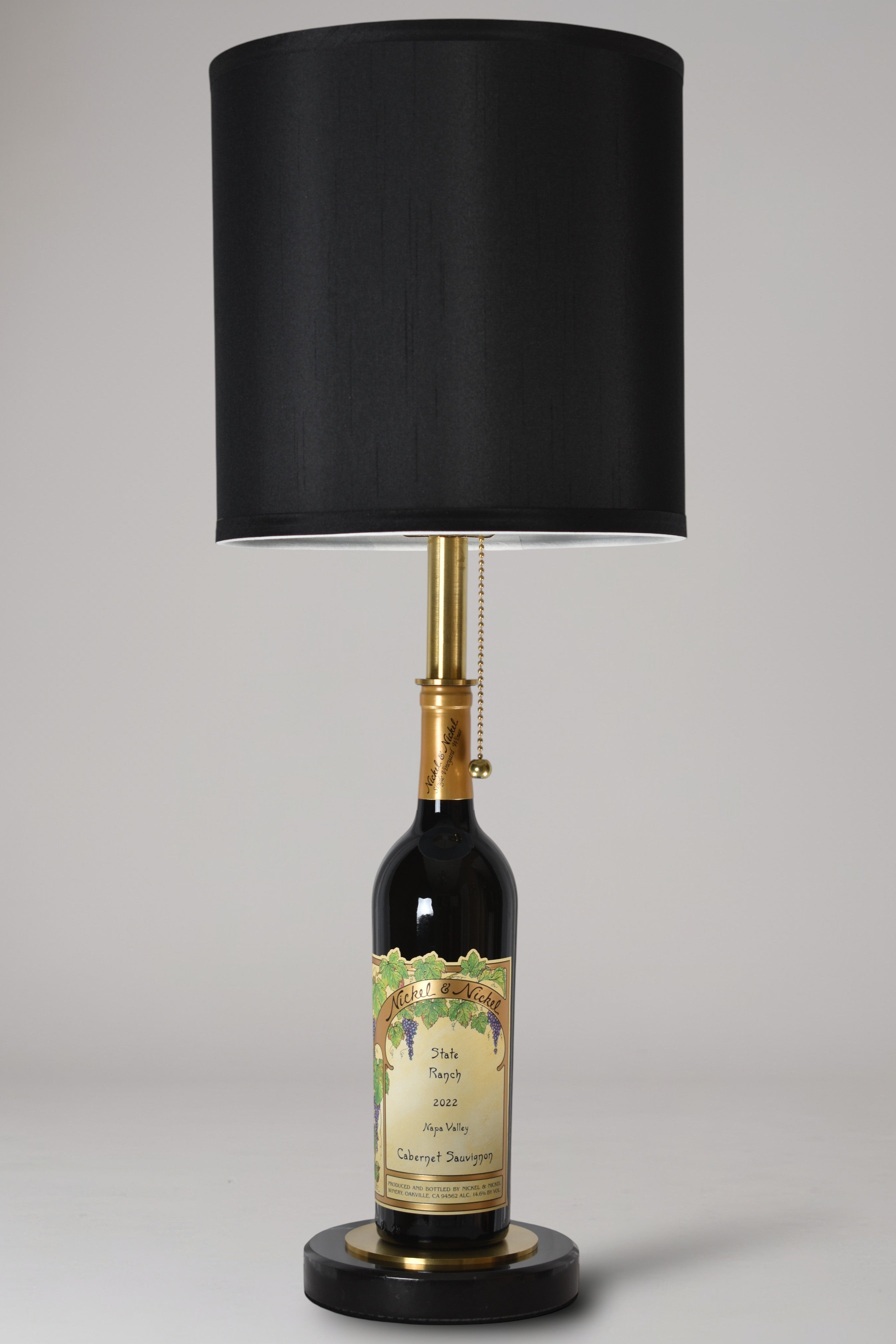 Wine bottle lamp made from a reclaimed 2022 Nickel & Nickel Cabernet Sauvignon bottle, full view, light off, on a gray background