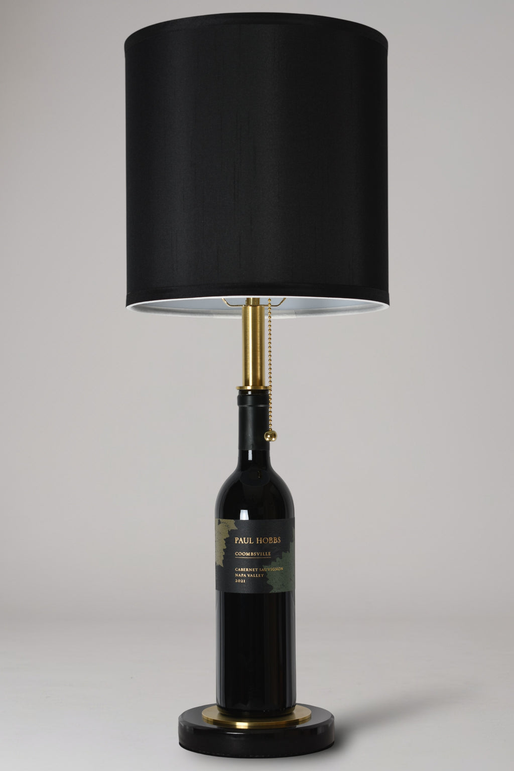 Wine bottle lamp made from a reclaimed 2021 Paul Hobbs Cabernet Sauvignon bottle, full view, light off, on a gray background