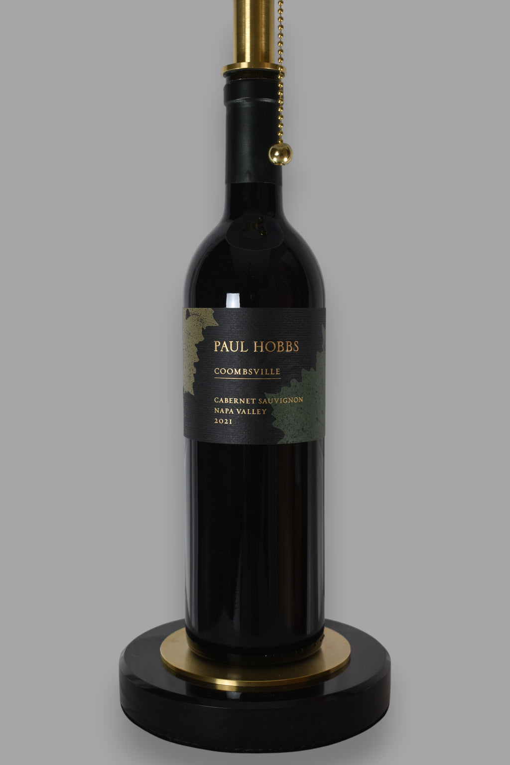 Wine bottle lamp made from a reclaimed 2021 Paul Hobbs Cabernet Sauvignon bottle, close-up view, on a gray background