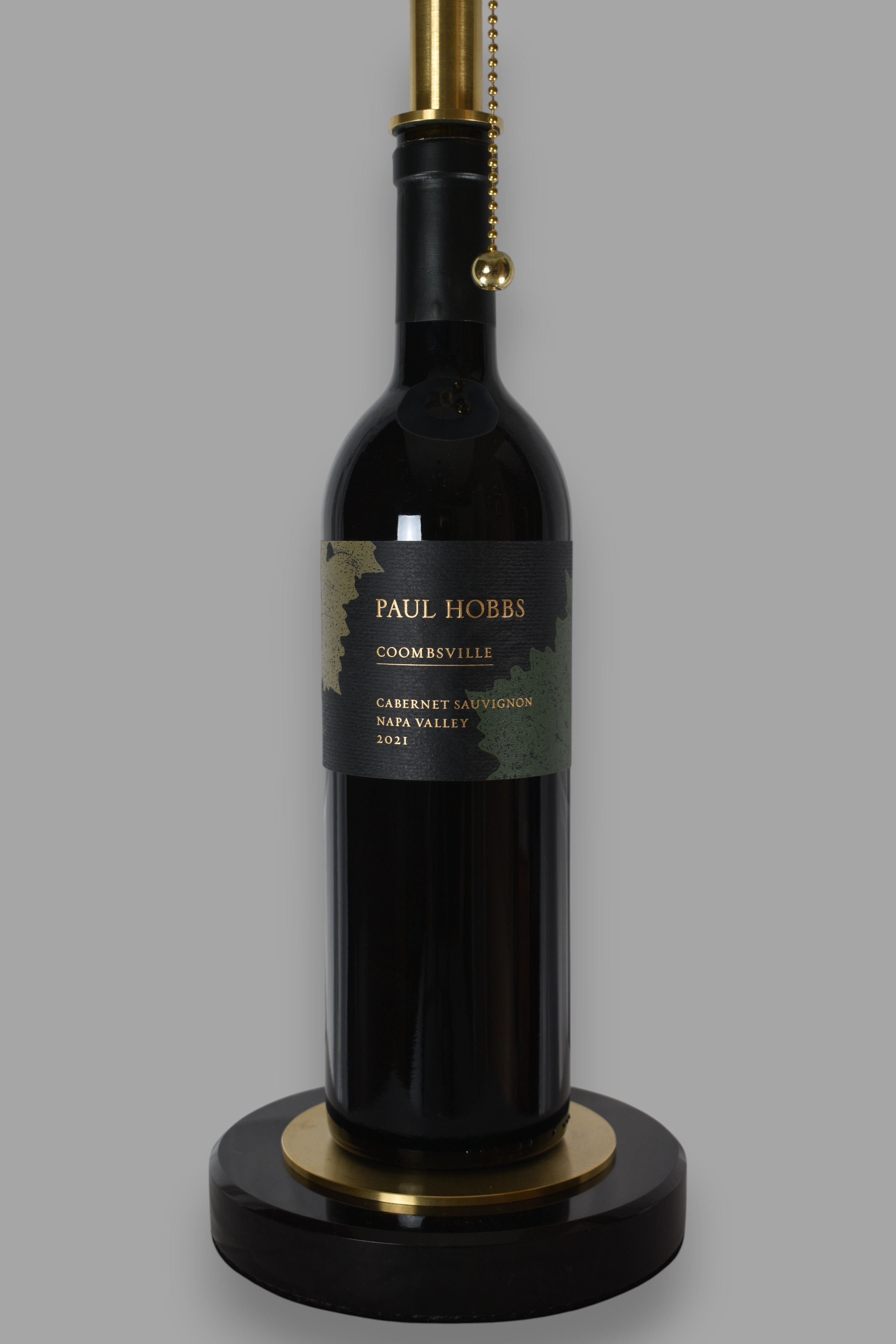 Wine bottle lamp made from a reclaimed 2021 Paul Hobbs Cabernet Sauvignon bottle, close-up view, on a gray background