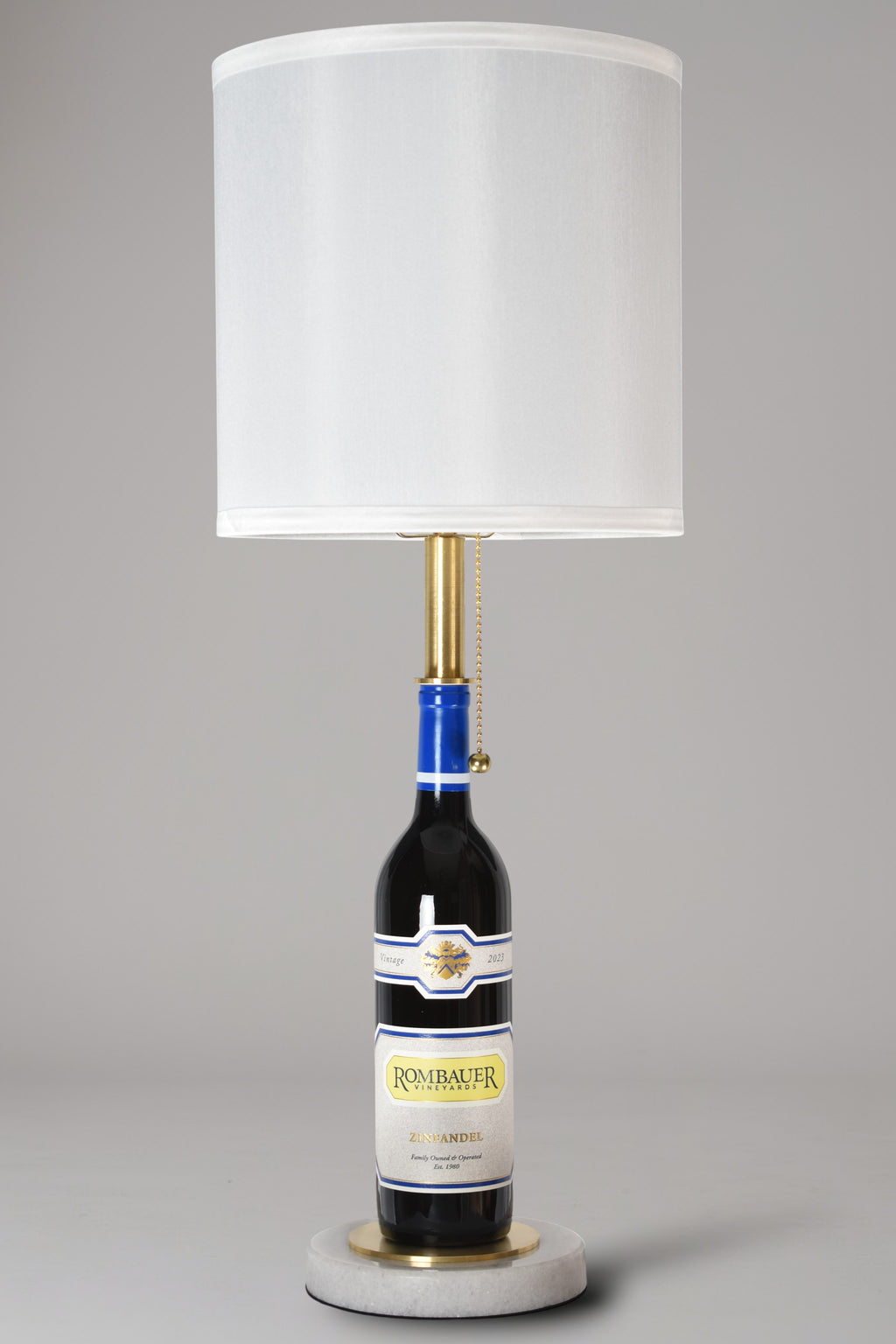 Wine bottle lamp made from a reclaimed 2023 Rombauer Zinfandel bottle, full view, light off, on a gray background