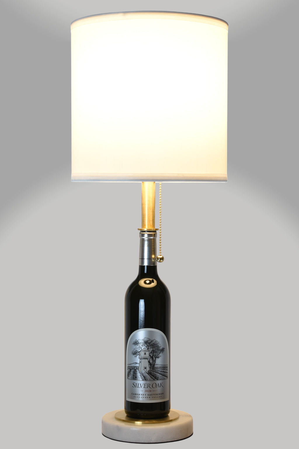 Wine bottle lamp made from a reclaimed 2020 Silver Oak Cabernet Sauvignon bottle, full view, light on, on a gray background