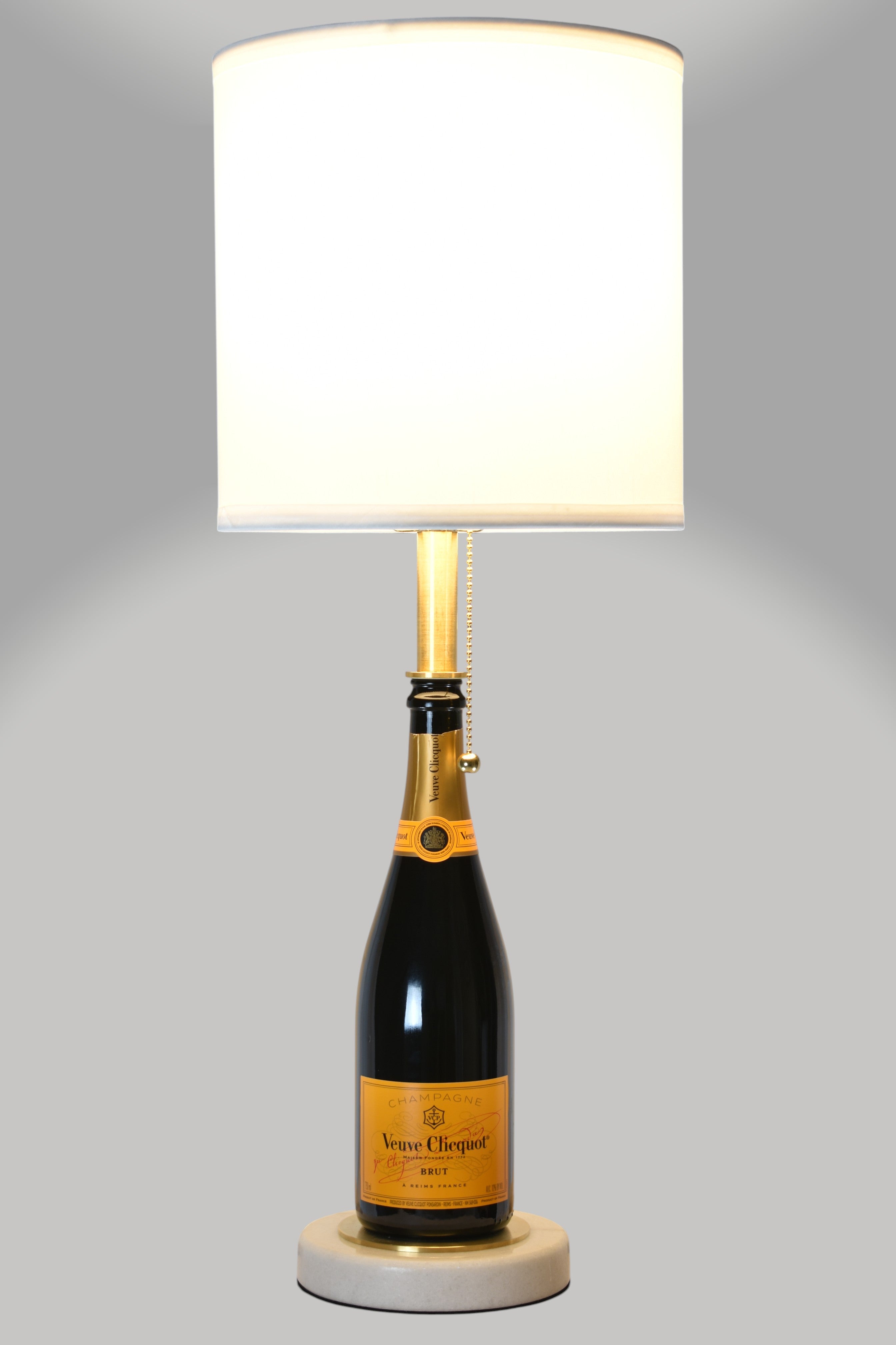 Wine bottle lamp made from a reclaimed Veuve Clicquot Brut Champagne bottle, full view, light on, on a gray background