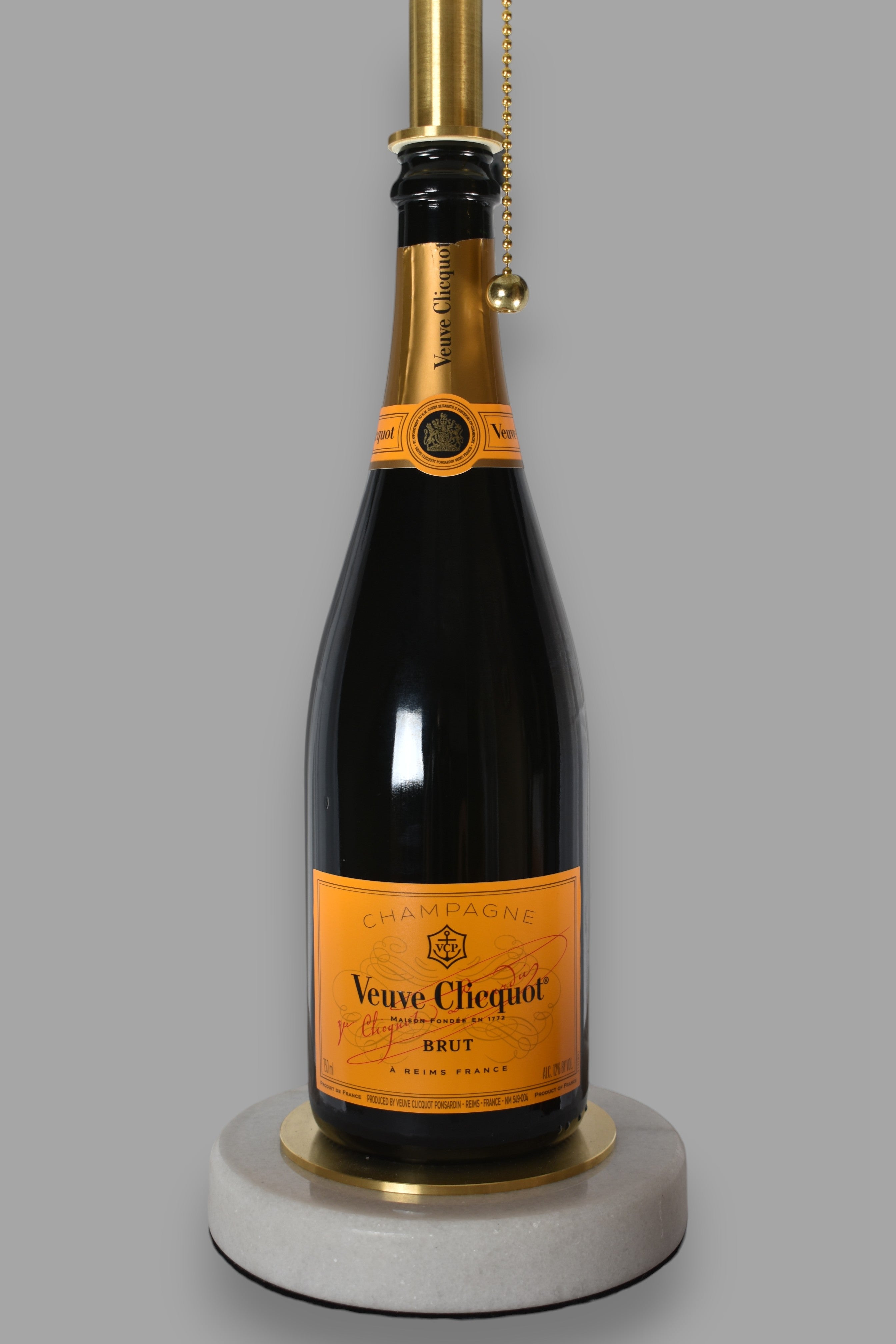 Wine bottle lamp made from a reclaimed Veuve Clicquot Brut Champagne bottle, close-up view, on a gray background